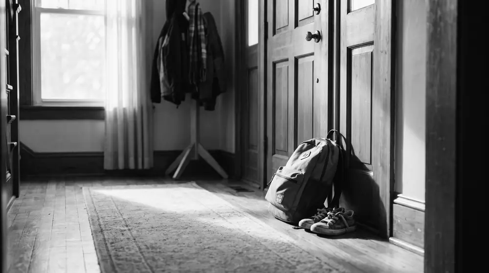 Mochila escolar y zapatillas de niño junto a la puerta de casa